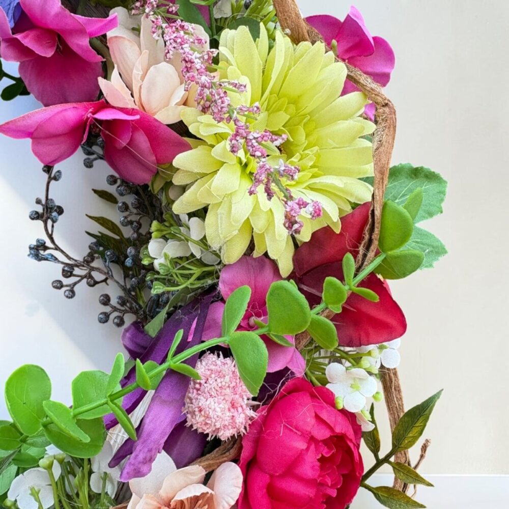 Kleurrijke zijden bloemenkrans Berry Gloss met roze, rode, blauwe en gele bloemen op natuurlijke takkenbasis.