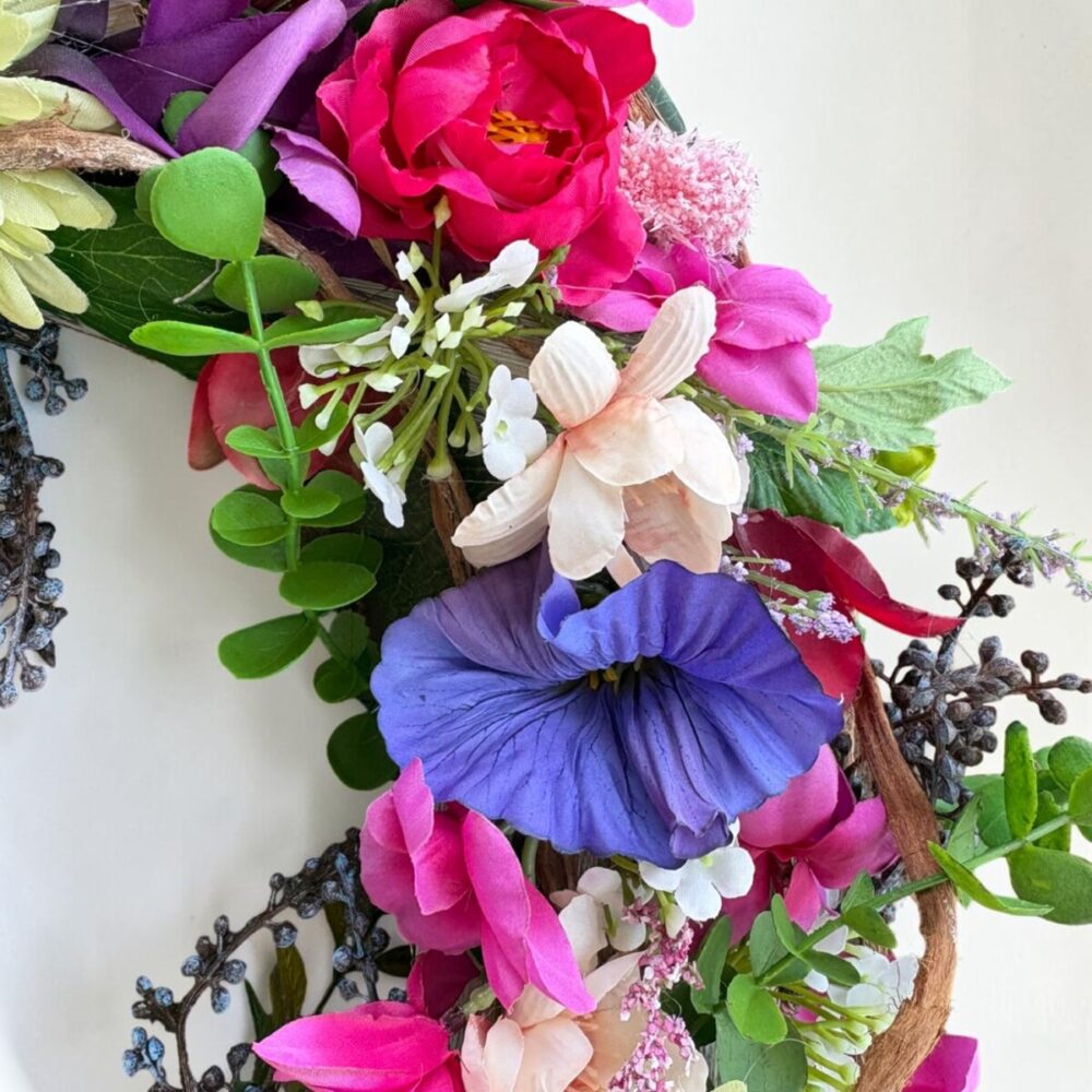Kleurrijke zijden bloemenkrans Berry Gloss met roze, rode, blauwe en gele bloemen op natuurlijke takkenbasis.