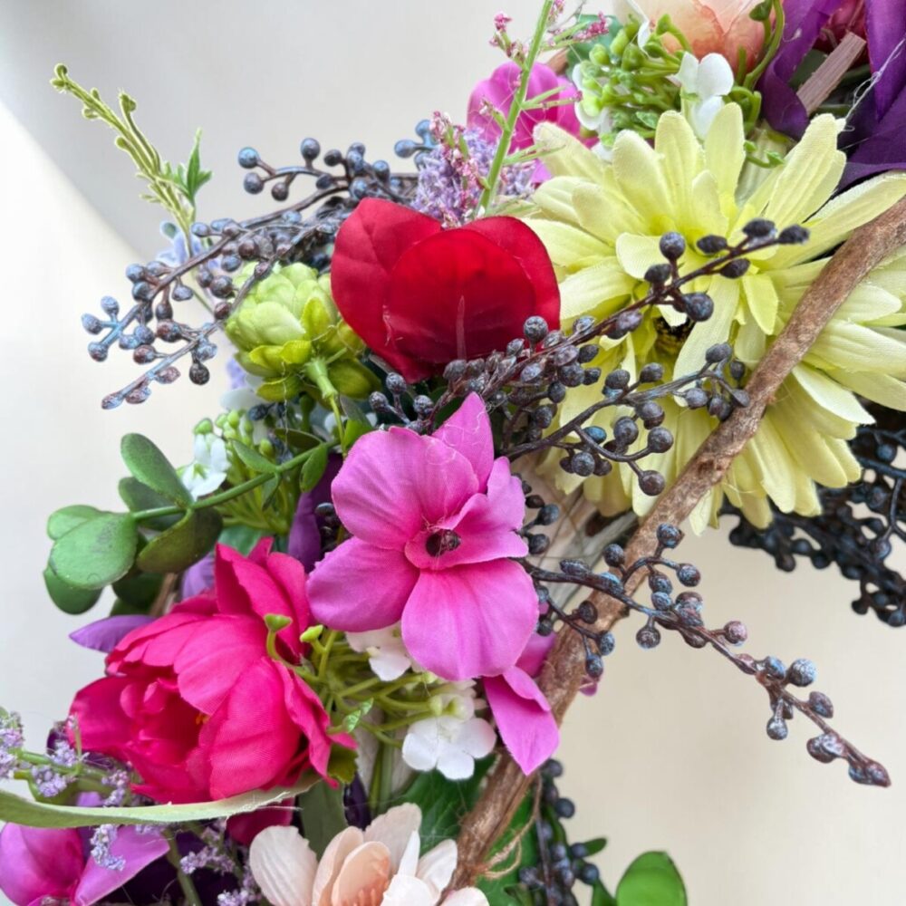 Kleurrijke zijden bloemenkrans Berry Gloss met roze, rode, blauwe en gele bloemen op natuurlijke takkenbasis.